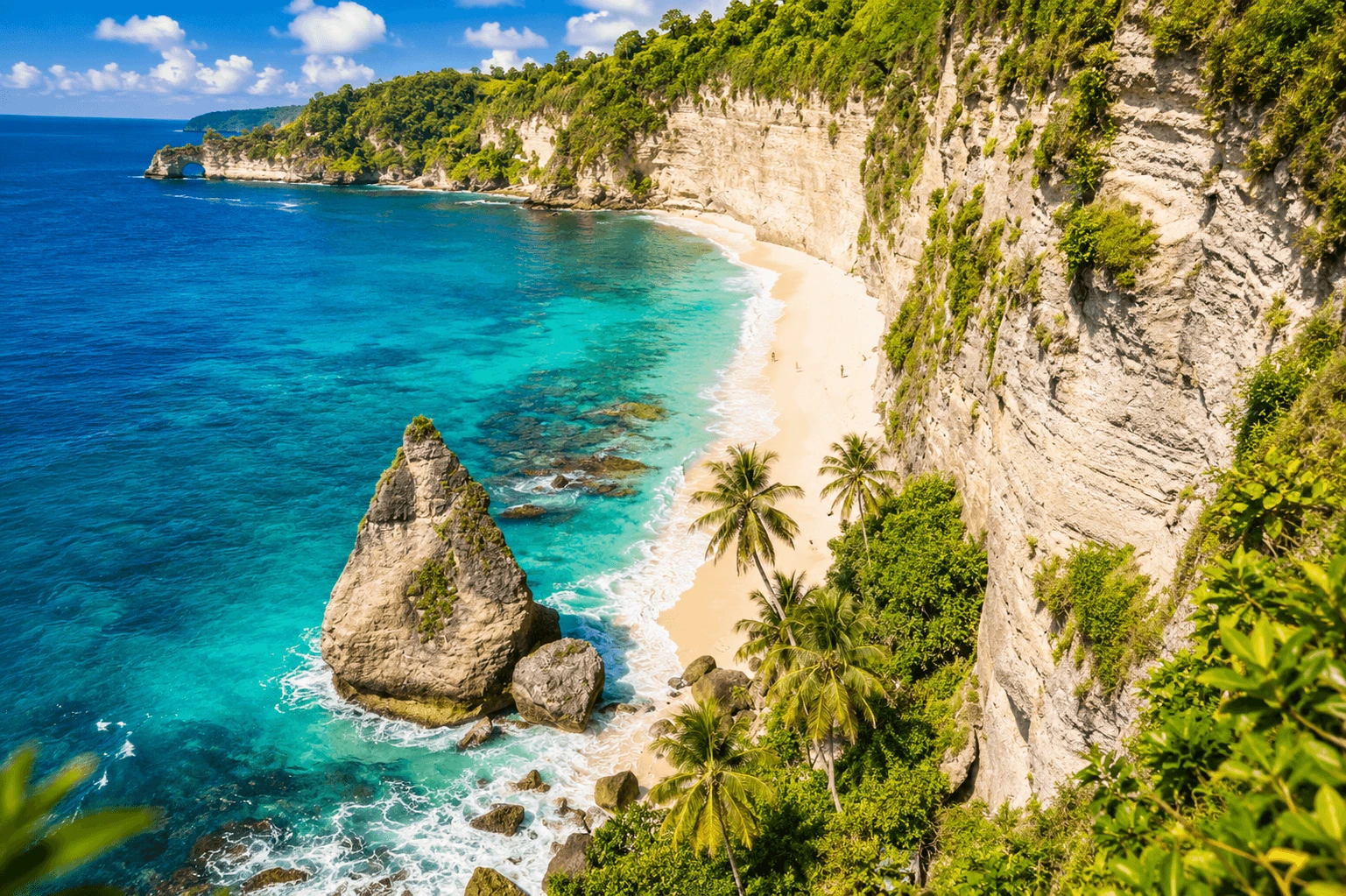 A stunning view of Diamond Beach featuring crystal-clear turquoise waters, towering limestone cliffs, white sandy shores, and dramatic tropical coastal scenery.