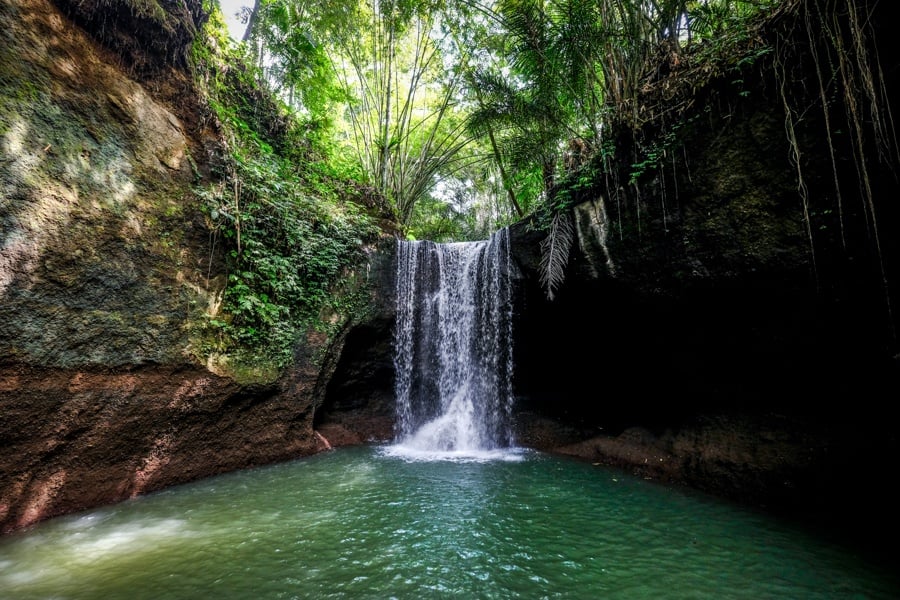A beautiful jungle view of Suwat Waterfall featuring cascading water flowing into a clear natural pool, surrounded by lush tropical greenery and a peaceful rainforest atmosphere.