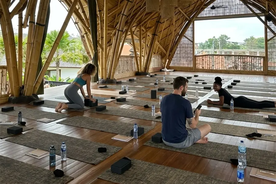 A hidden yoga center in Bali surrounded by lush tropical greenery, peaceful jungle scenery, and open-air wooden yoga spaces, creating a calm and natural atmosphere perfect for relaxation and meditation.