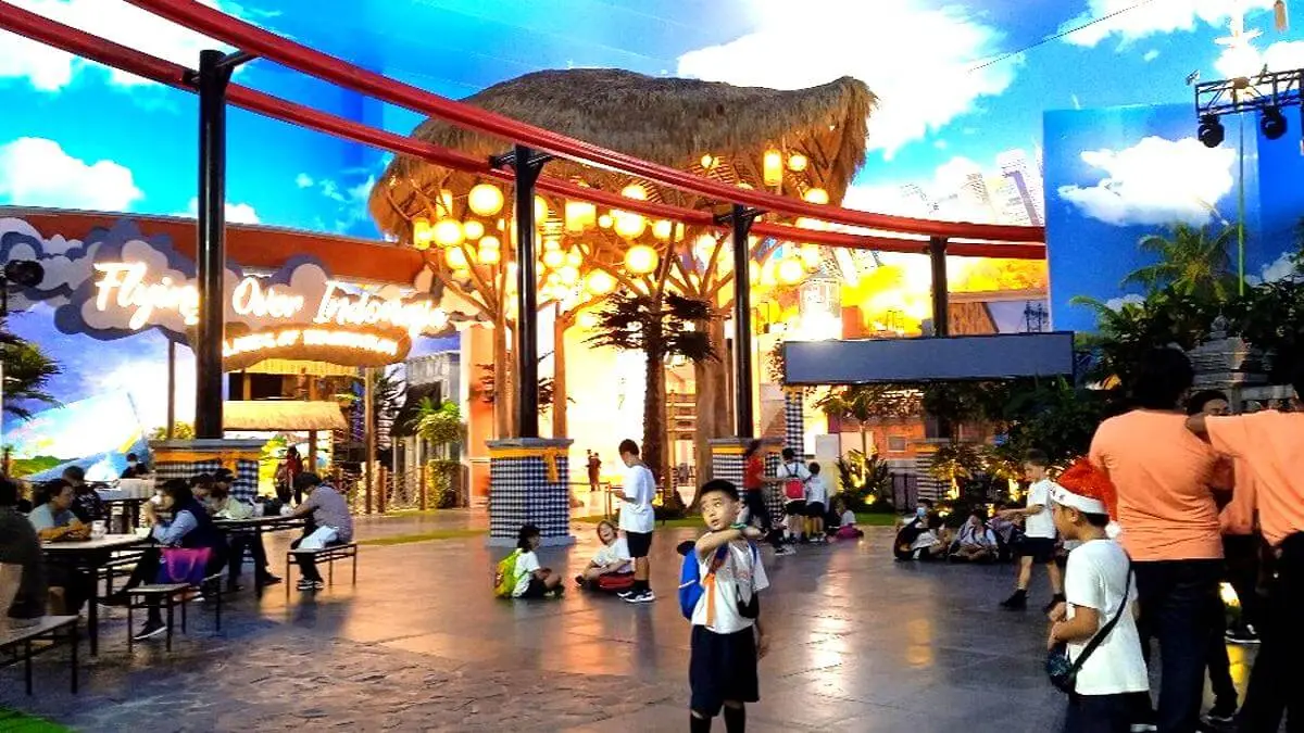 A lively scene at Trans Studio Mall Bali with groups of school children on a field trip, sitting together in uniform while exploring the modern shopping complex and enjoying an educational outing.
