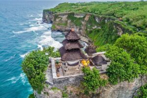 A sweeping view of a historic sea temple built on the edge of a high cliff overlooking crashing ocean waves, a classic choice among bali tourist spots. | balitouristic.com