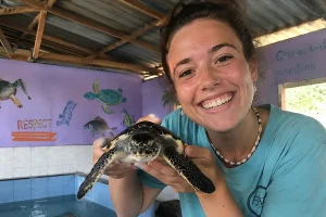 A visitor smiling while safely holding a large green sea turtle at the turtle island bali sanctuary, highlighting the unique wildlife encounters available | balitouristic.com