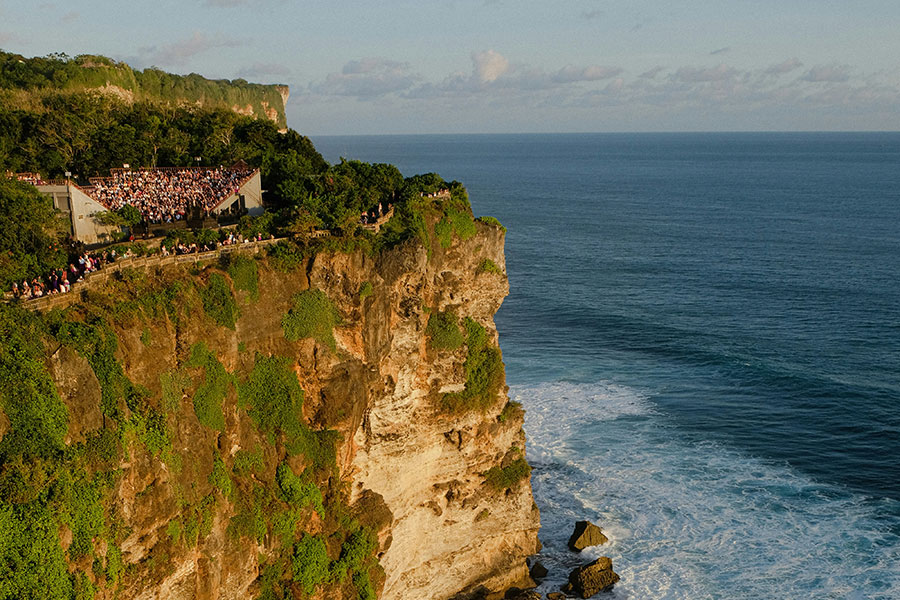 A breathtaking view from the cliffs of Uluwatu Temple during a Tanah Lot Sunset Tour, featuring dramatic limestone cliffs, endless Indian Ocean vistas, golden sunset light, and travelers admiring one of Bali’s most spectacular coastal landscapes.
