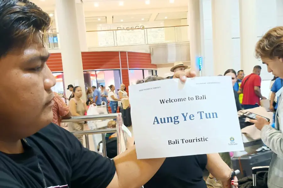 A friendly local driver greeting international tourists at the airport arrivals area for their premium bali airport transfer to seminyak. | balitouristic.com