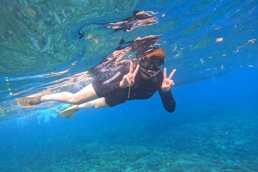 A tourist happily making a peace sign while exploring vibrant marine life during a blue lagoon snorkeling adventure. | balitouristic.com