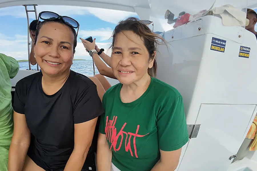 Two happy friends relaxing inside a covered speedboat during their convenient and organized blue lagoon snorkeling excursion. | balitouristic.com