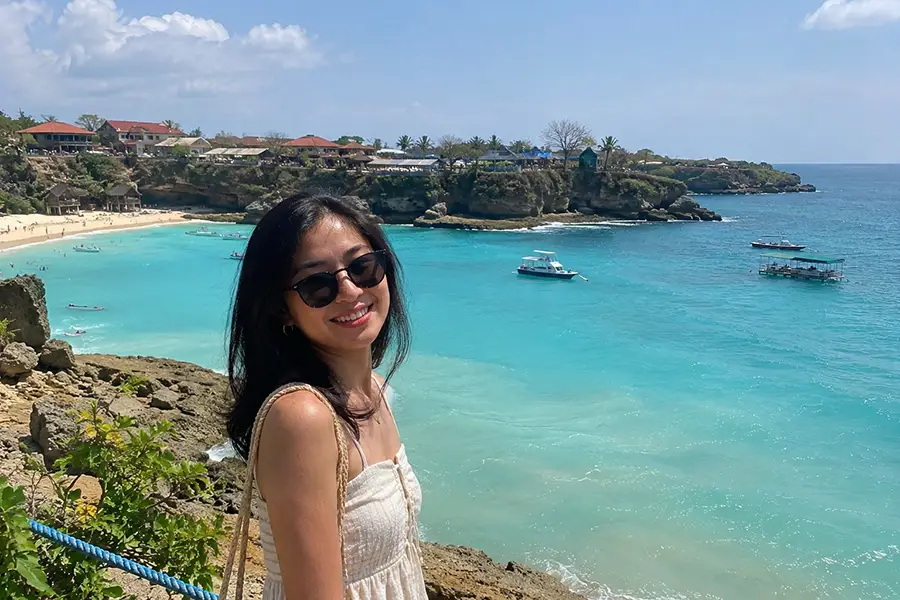 A tourist posing against the backdrop of a bright blue tropical bay and coastal cliffs during a nusa lembongan day trip | balitouristic.com