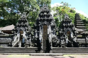 Three traditional split stone gates (Candi Bentar) with detailed relief carvings standing prominently in a row on the grounds of goa lawah temple.