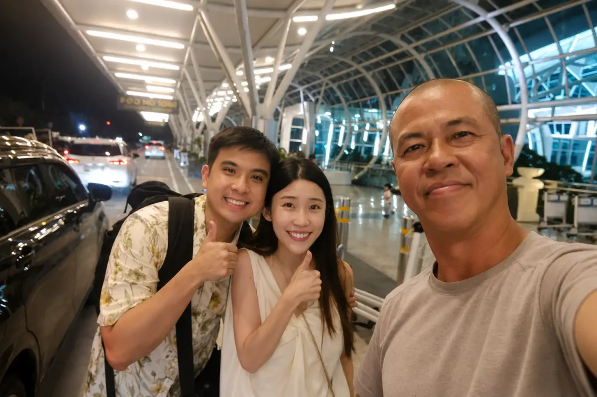 A friendly local driver from an airport transfer company warmly welcoming a couple of tourists from Singapore at Ngurah Rai International Airport, assisting with their luggage and creating a comfortable, professional, and stress-free start to their Bali vacation.