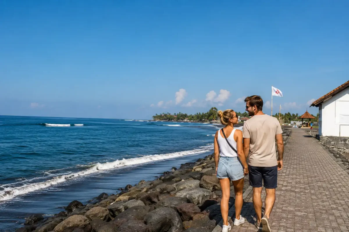 A happy couple walking hand in hand along the black sand shoreline of Lebih Beach, surrounded by gentle ocean waves, dramatic coastal scenery, swaying palm trees, and warm golden sunlight, creating a peaceful and romantic tropical atmosphere.