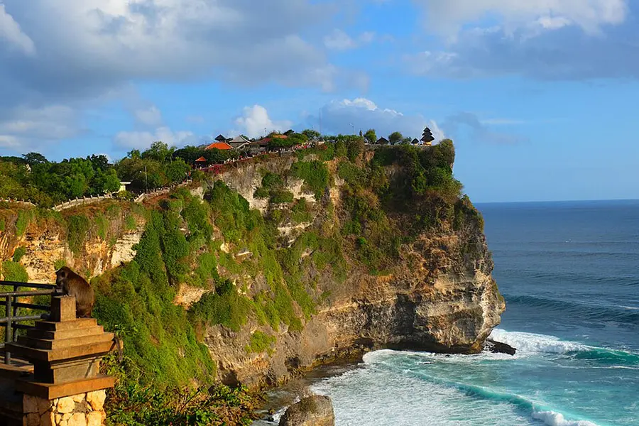 A sweeping view of a historic sea temple built on the edge of a high cliff overlooking crashing ocean waves, a classic choice among bali tourist spots.