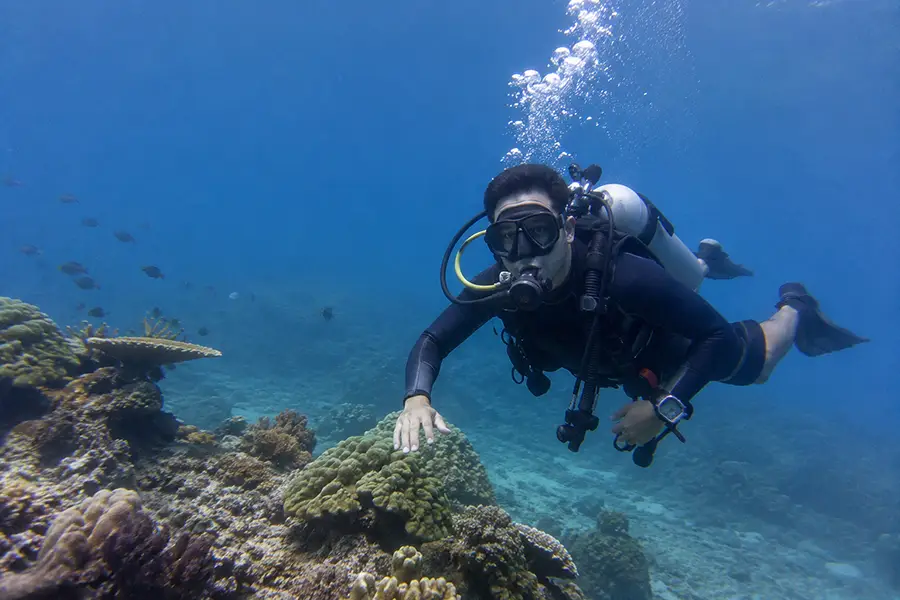 A scuba diver swimming gracefully underwater over vibrant coral formations with air bubbles floating to the surface during a bali jet set dive experience.