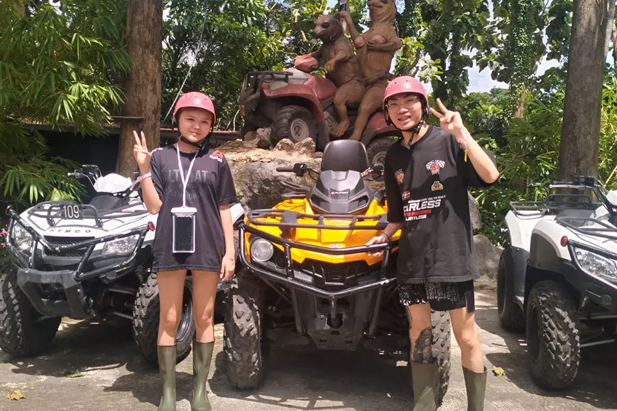 A young couple wearing safety helmets and tall rubber boots posing together next to an outdoor quad bike before their ride, featured in action-packed bali packages for couple.