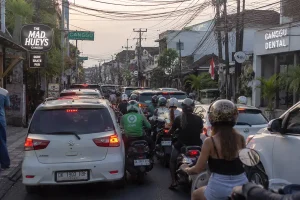 A long line of cars and scooters gridlocked on a narrow urban street next to popular local boutiques, a common sight solved by effective bali traffic tips.