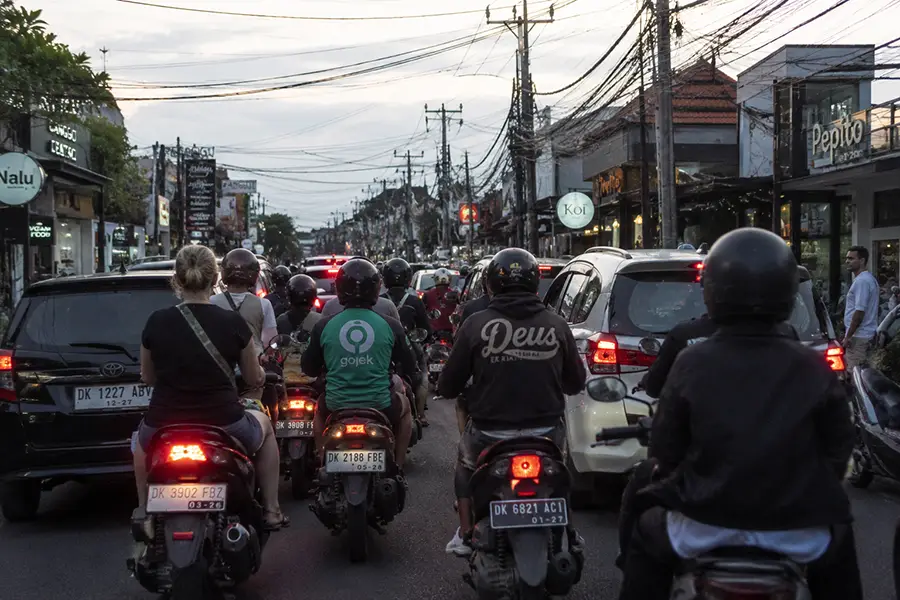 Motorbikes and cars tightly packed together in a slow-moving street lane at dusk, illustrating the realistic road conditions handled by helpful bali traffic tips.