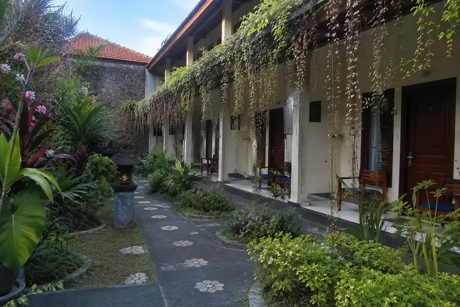 A happy tourist couple enjoying their stay at a cozy budget accommodation Bali, relaxing by a tropical garden and swimming pool with modern yet affordable rooms, warm morning sunlight, and a peaceful island atmosphere that combines comfort, value, and authentic Balinese hospitality.