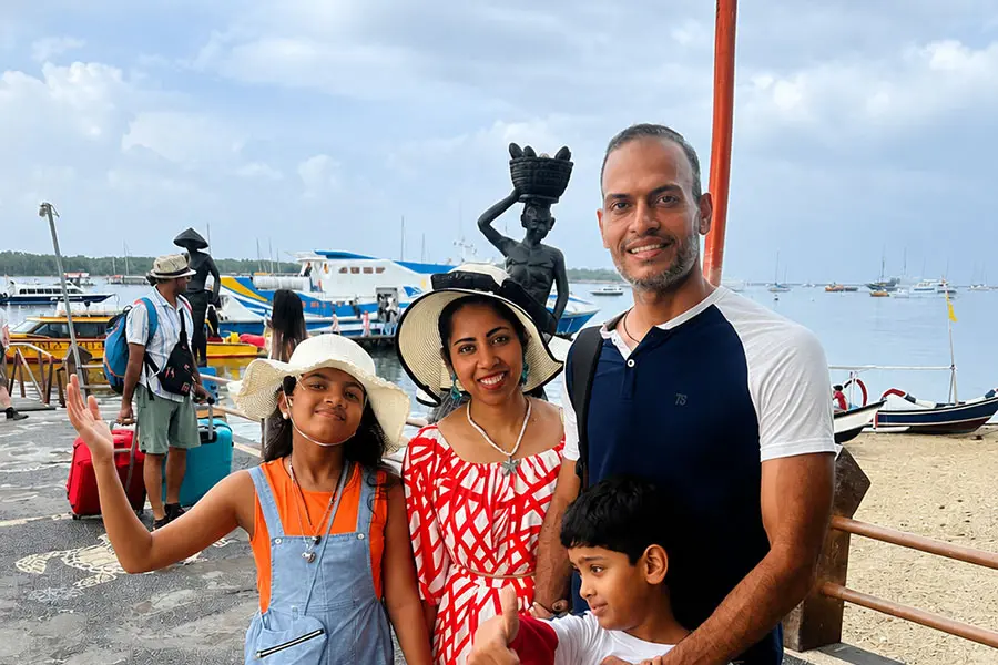 A happy tourist family posing together near a tropical boat harbor before starting their custom day trip to hire bali driver ubud. | balitouristic.com