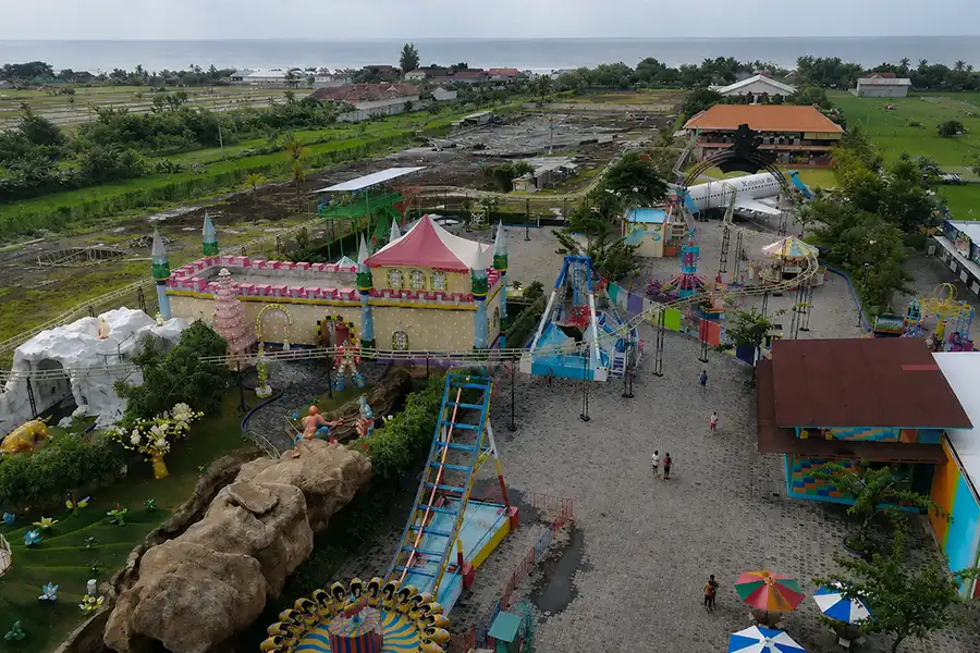 krisna funtastic land - buleleng interesting places to visit - bali touristic An overhead high-angle view showcasing various colorful rides, a castle, and an airplane replica at krisna funtastic land near the coastline. | balitouristic.com