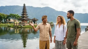 A happy tourist couple enjoying a private tour at Ulun Danu Beratan Temple, walking hand in hand along the lakeside temple grounds with a friendly local guide, surrounded by misty mountains, tranquil waters, vibrant gardens, and traditional Balinese architecture in a peaceful tropical atmosphere.
