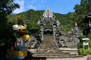 Wide stone steps leading up to an intricately carved black stone gateway set against a lush green hill at pulaki temple.