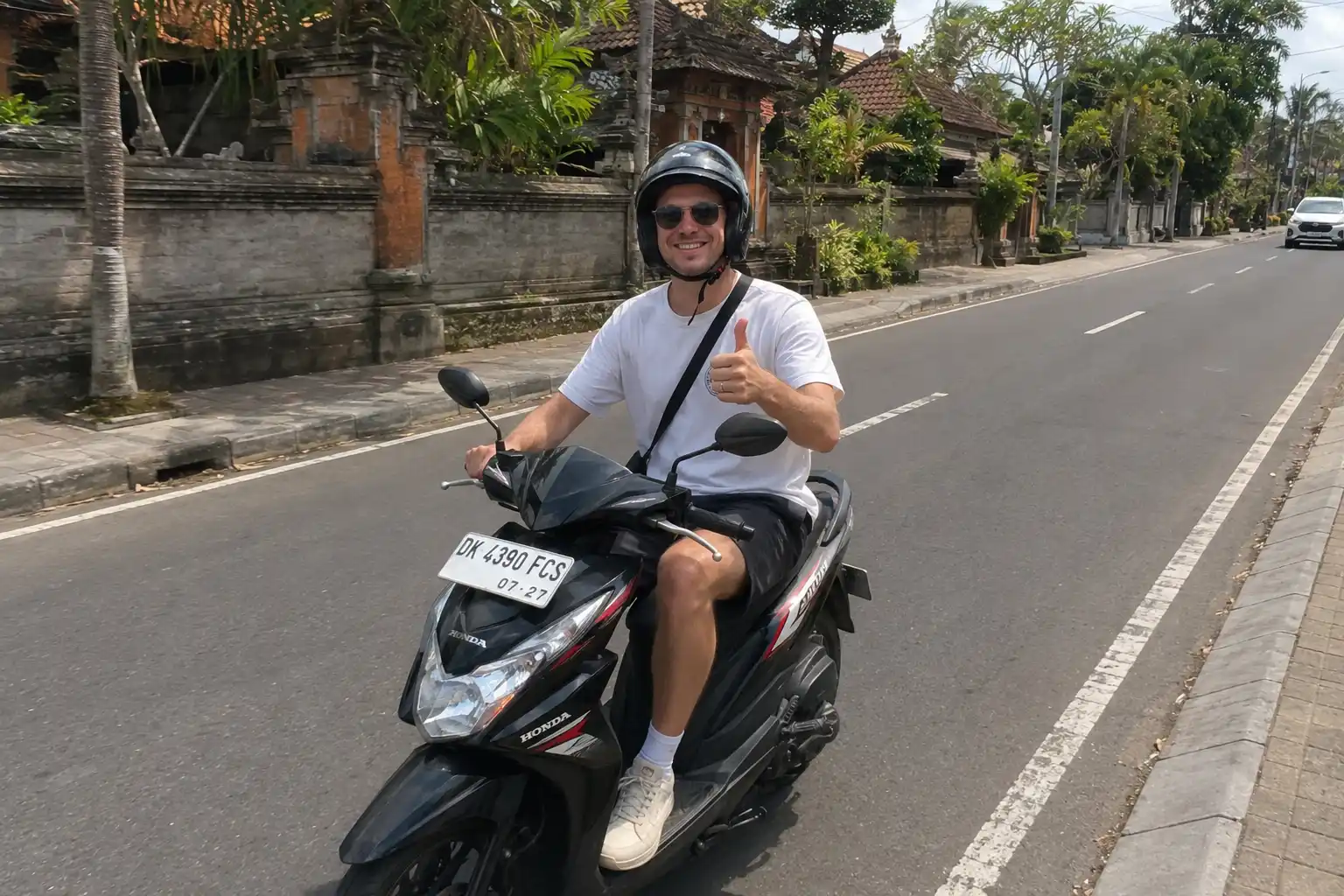 A male tourist smiling and giving a thumbs-up while riding a black Honda automatic motorbike, showing a popular choice for scooters in bali. | balitouristic.com