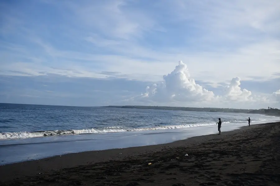 Silhouettes of local fishermen casting their fishing rods into the ocean waves along the exotic black sand shoreline of sedayu beach.