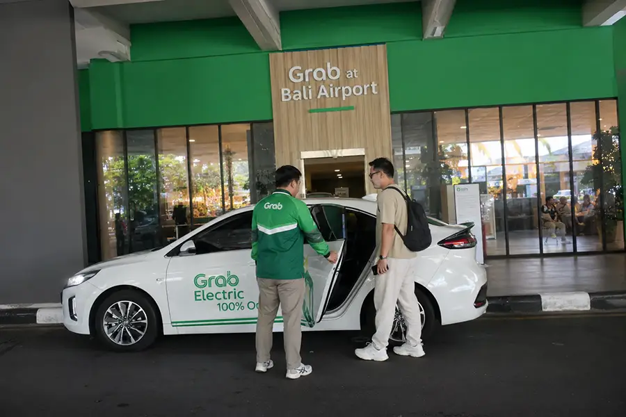 A passenger getting into a white Grab Electric car with a driver opening the door at the official Grab zone, representing a convenient taxi airport bali option. | balitouristic.com