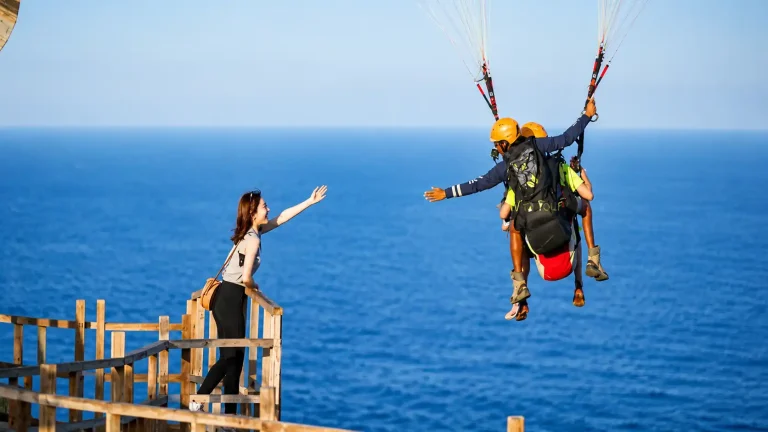 Adventure seekers enjoying paragliding in Bali, soaring high above crystal-clear ocean waters with colorful parachutes, breathtaking coastal views, tropical beaches, and an exciting water sports atmosphere.