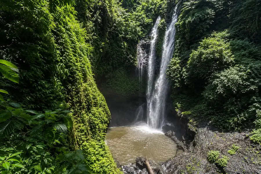 A tall, powerful waterfall plunging into a deep pool surrounded by steep jungle canyon walls.