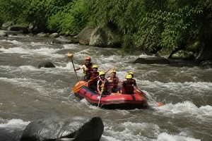 Tourists wearing yellow helmets paddling a red inflatable raft down rushing river rapids.