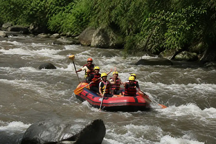 Tourists wearing yellow helmets paddling a red inflatable raft down rushing river rapids.