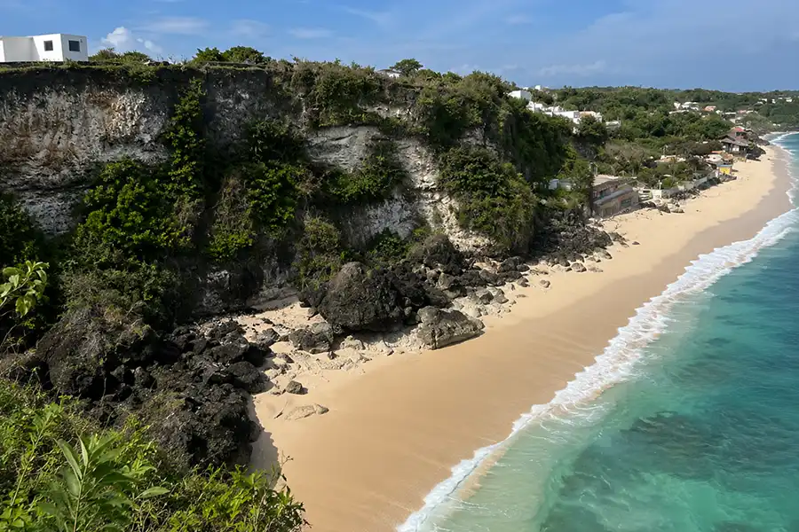 High-angle panoramic view of a golden sand beach beneath limestone cliffs meeting turquoise ocean water.