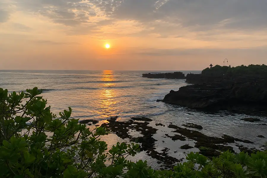 Ocean waves crashing against dark rocky cliffs at sunset under a warm orange-lit sky.