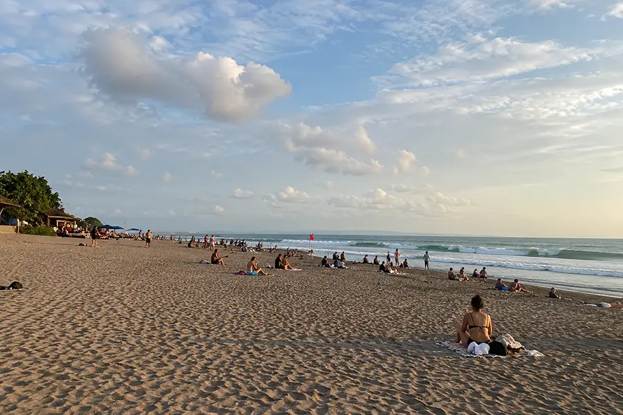 Tourists relaxing on a wide sandy beach as gentle ocean waves lap against the shore.