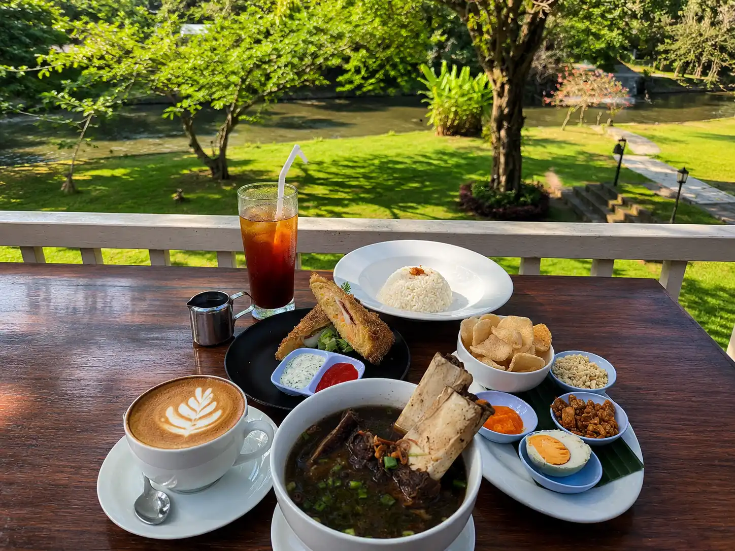 A table filled with Balinese ribs soup, rice, side dishes, iced tea, and a hot latte.