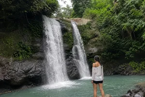 A woman standing near the water looking at twin waterfalls flowing down dark rock walls into a turquoise pool.