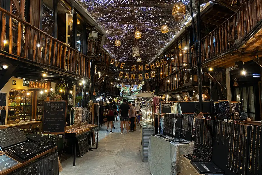 A vibrant indoor boutique market with wooden stalls, hanging warm lamps, and handicraft displays.