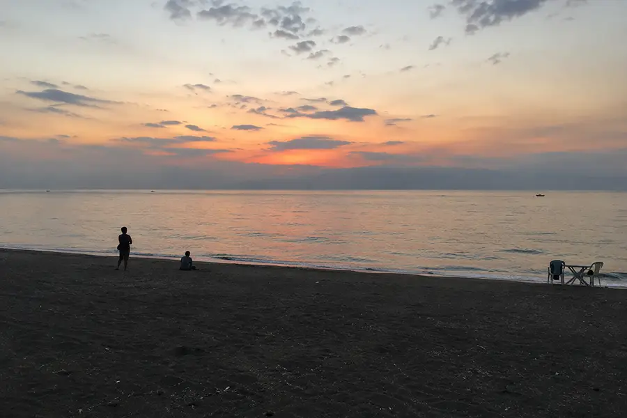 Silhouettes of visitors standing on the quiet dark sand beach looking out at the ocean sunset.