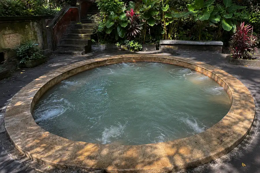 A round warm stone pool surrounded by lush tropical plants and stone steps.