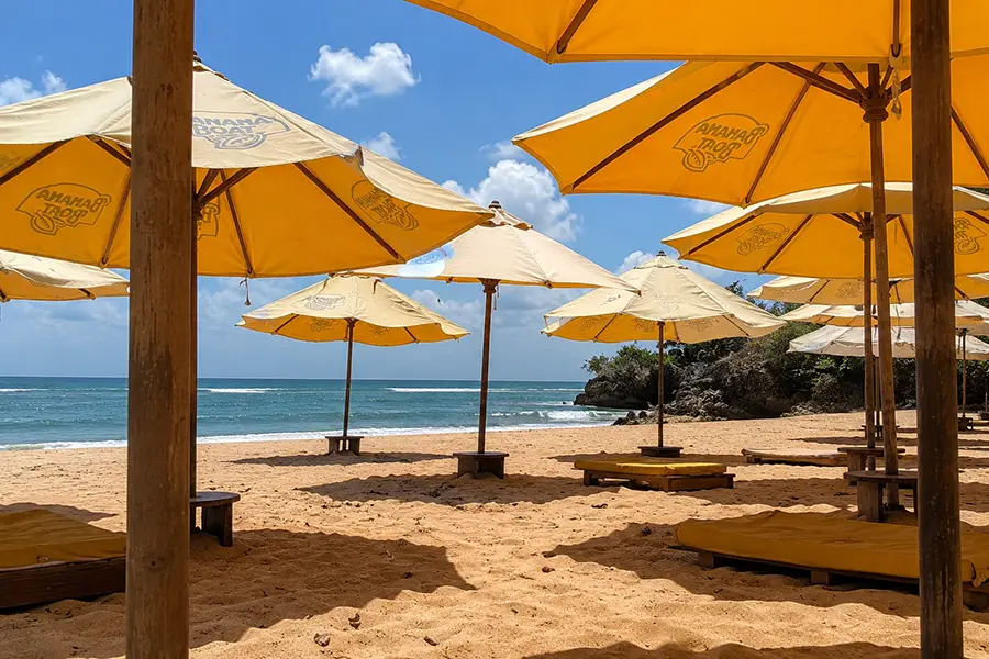 Yellow beach umbrellas and wooden sunbeds arranged on golden sand overlooking turquoise ocean waves.