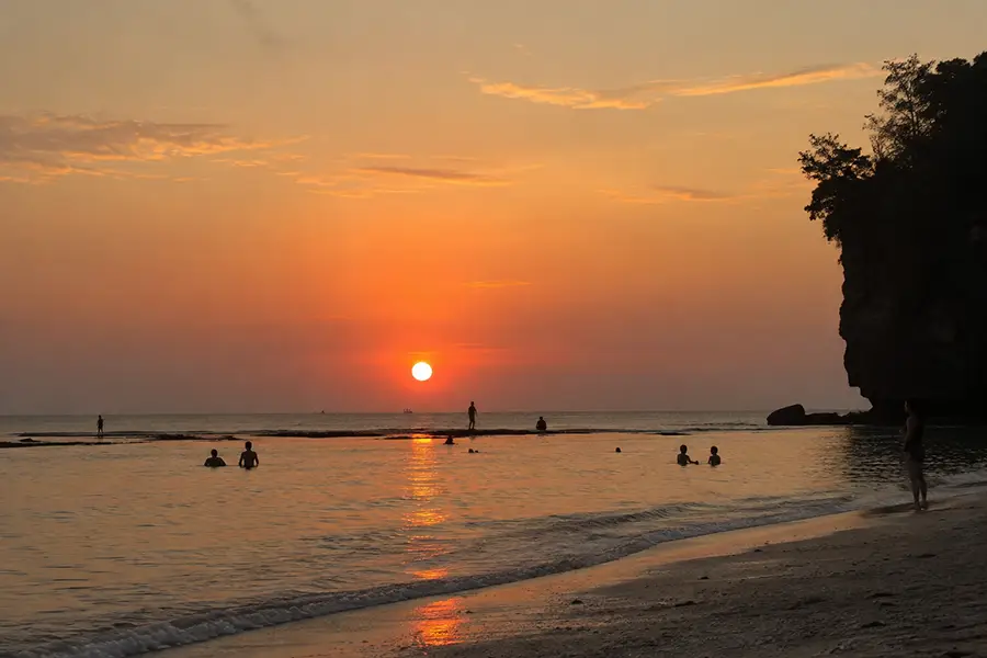 People relaxing in the calm ocean water during a golden sunset at Padang Padang Beach Uluwatu.