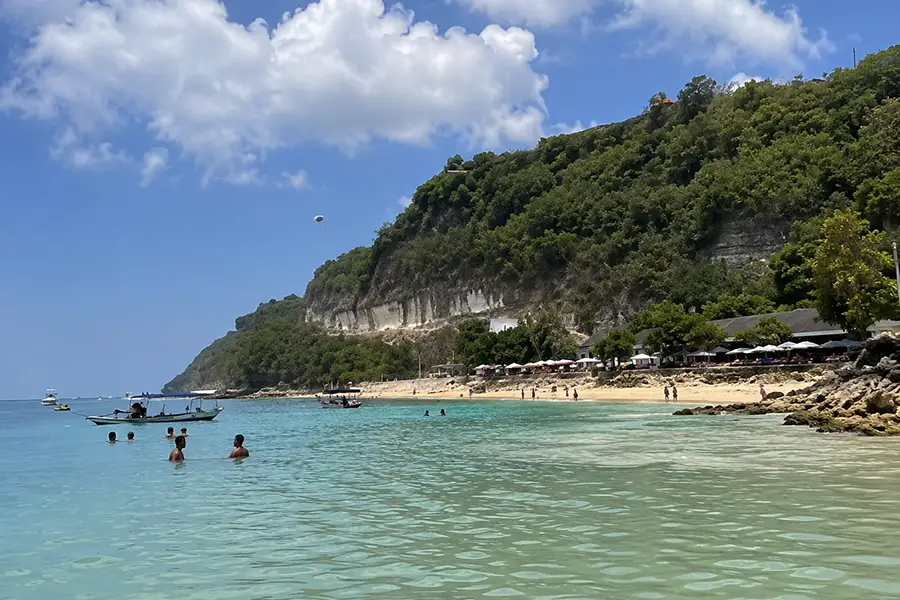 Visitors relaxing in a shallow water channel surrounded by limestone rocks and kayaks leading out to the blue ocean.