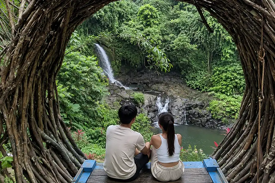 A couple sitting inside a circular wooden bird's nest frame looking out over a waterfall valley.