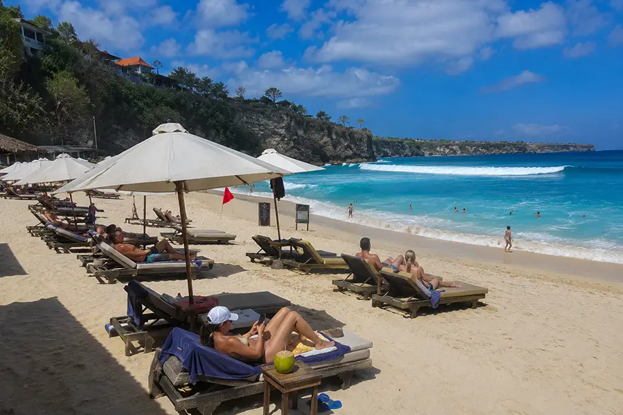 Tourists relaxing on sun loungers on a sandy beach.