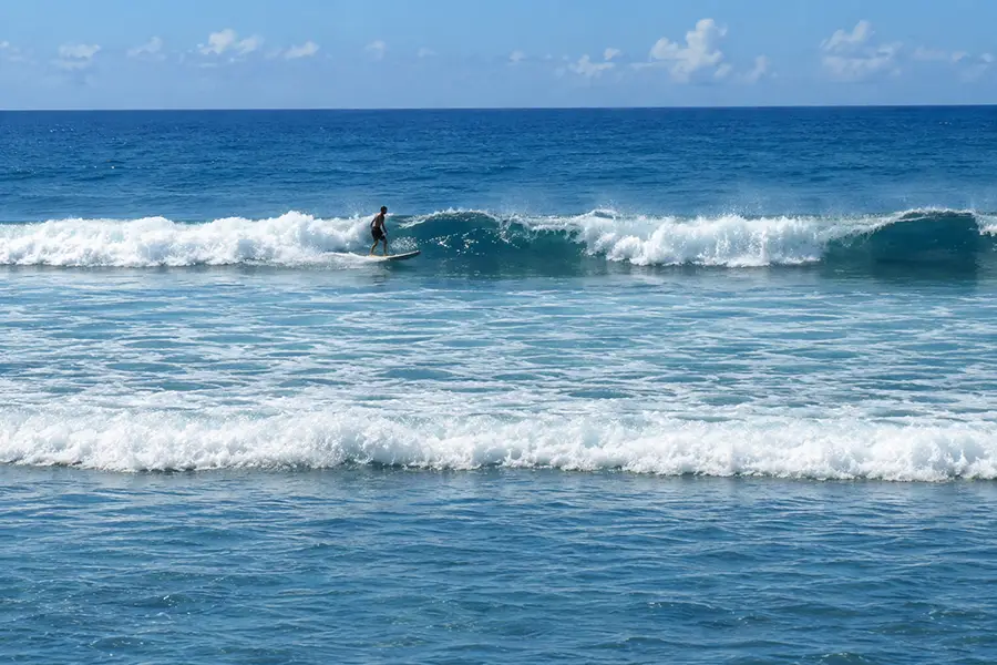 A surfer riding a rolling blue ocean wave under a bright clear sky.