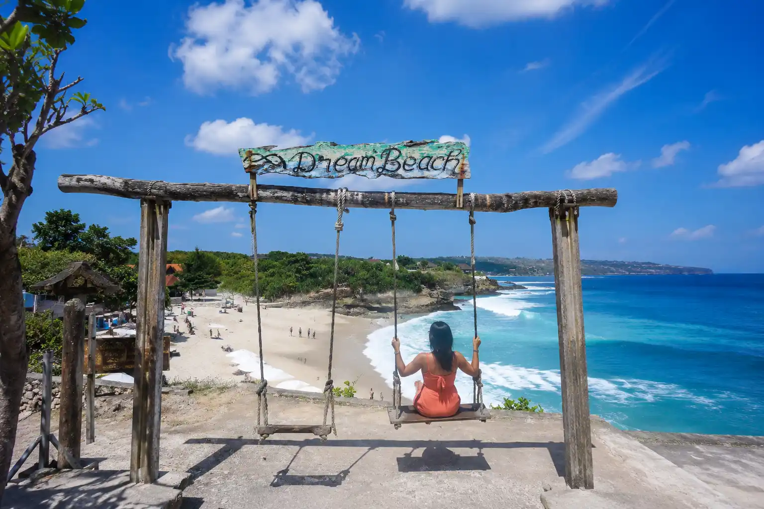 A woman on a swing overlooking a turquoise bay.