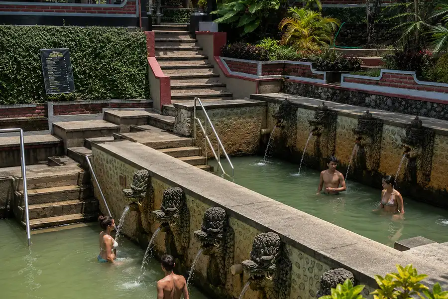 Visitors soaking in a hot spring pool under water flowing from carved dragon stone spouts.
