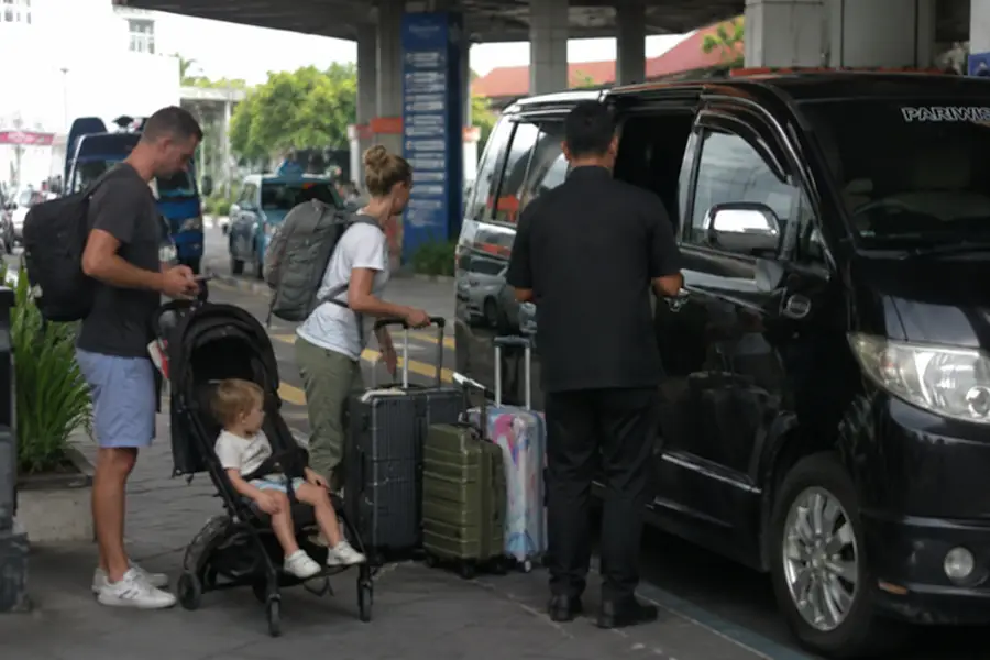 A family with a young toddler in a stroller loading their luggage into a black private van for a reliable bali airport transfer with baby seat.