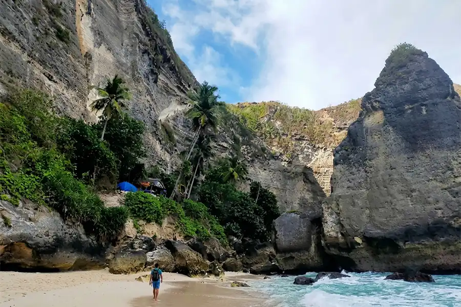 A traveler walking on the sandy shore of Diamond Beach beneath massive limestone cliffs.