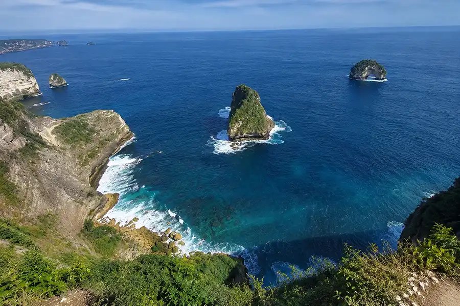 A high-angle scenic view of towering coastal cliffs and rock pillars rising from a turquoise sea.